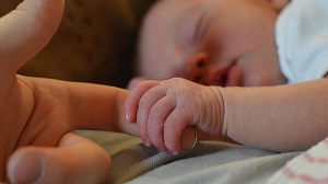 Imagem de um bebê segurando o dedo de um adulto